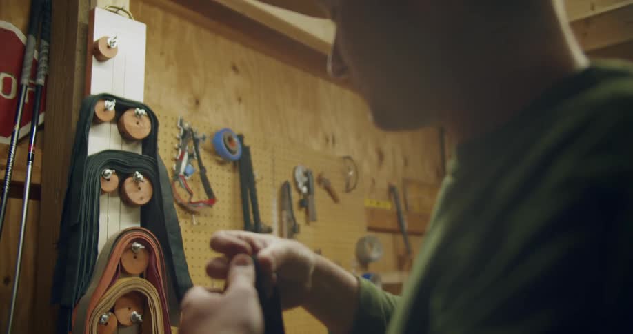 A man takes a belt off of a hanger with other belts and intends to fix something he is working on