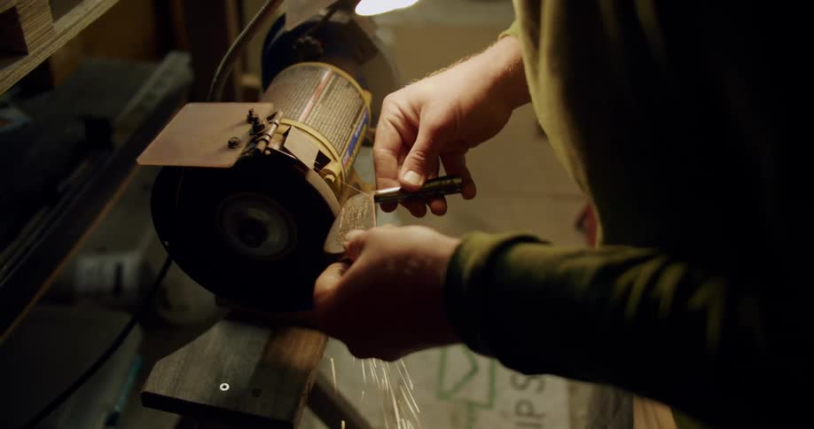 A man holds a golf putter against a grinding tool