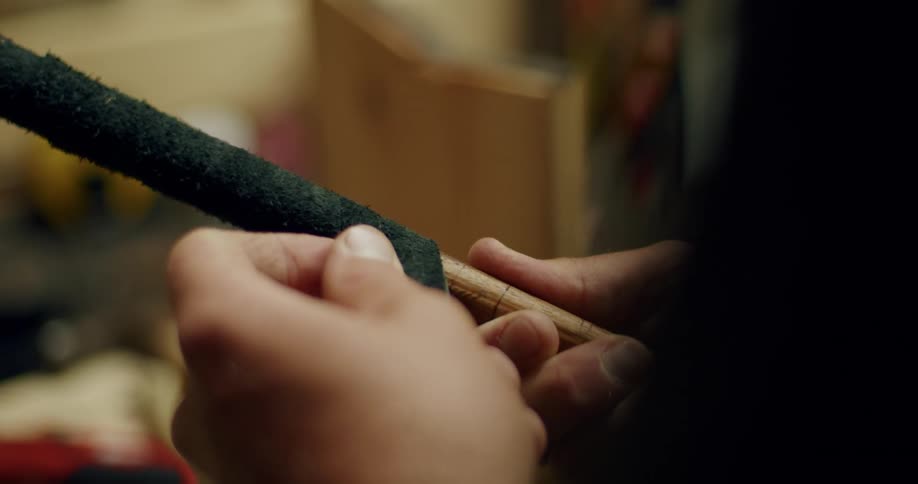 A man wraps a textured tape around a wooden stick