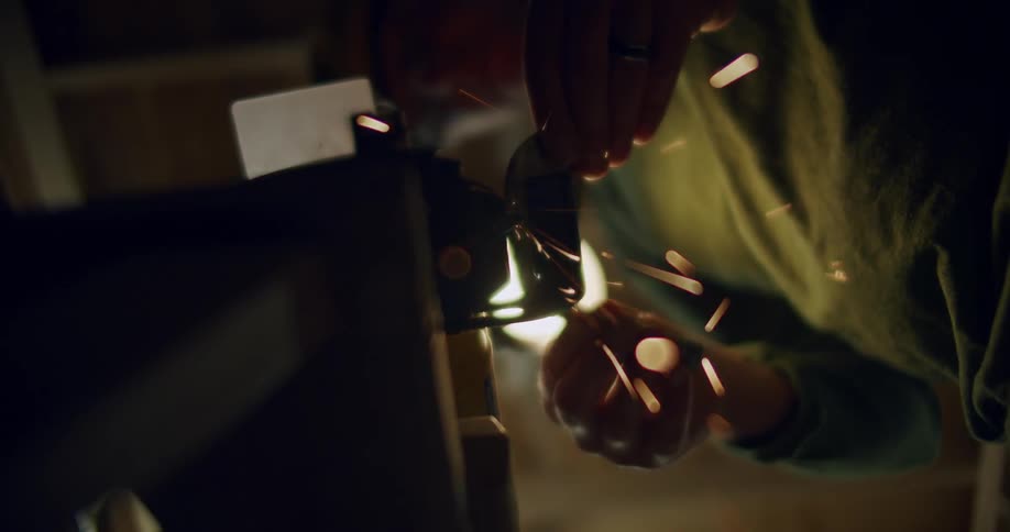 An up clsoe of a man grinder something small on a machine creating sparks