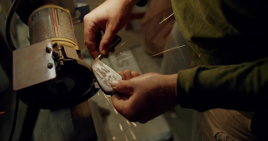 A close up of a man grinding a golf club head on a grinder