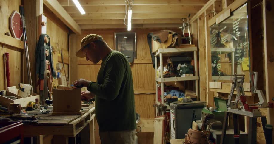 A man in a workshop wearing a cap works on a wooden box