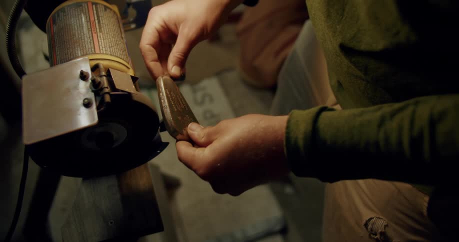 Man standing barefoot in workshop moves golf club head against grinder creating sparks