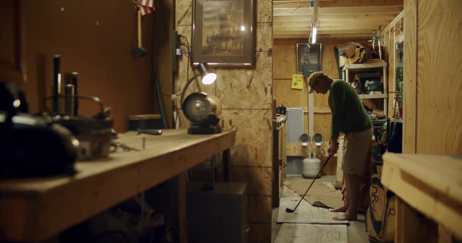 A man in a work shop testing a golf club looking at it and setting it down