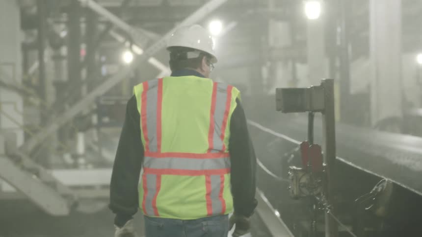 A workman is walking along moving machinery as water is spraying