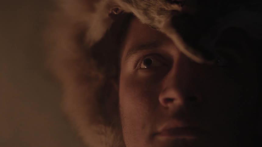 Man with animal pelt on his head staring off