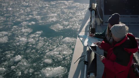 Two people examine a map on the rail of a ship