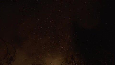 Smoke and embers from a fire rise into the night sky