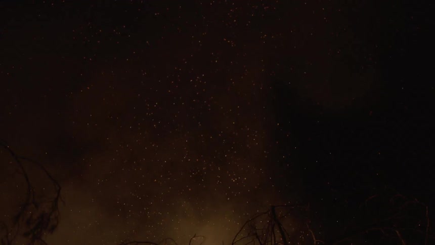 Smoke and embers from a fire rise into the night sky