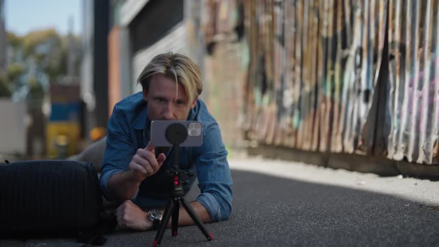 A man is lying in an alley looking through a camera on a tripod