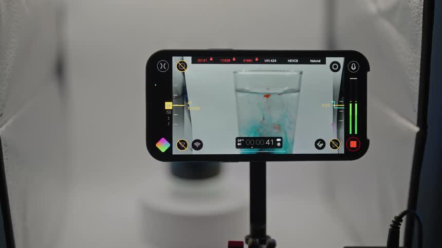 A smartphone being used as a camera to film a pill falling into a glass of water