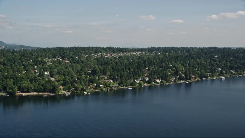 Aerial footage showcasing waterfront homes with piers nestled amongst wooded lots along the shores of Lake Washington in Mercer Island Washington on a sunny day