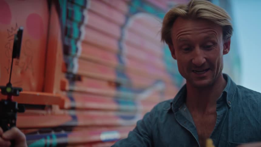 Blonde man with blue shirt makes video call with smartphone showing a bowl of french fries next to wall with graffiti
