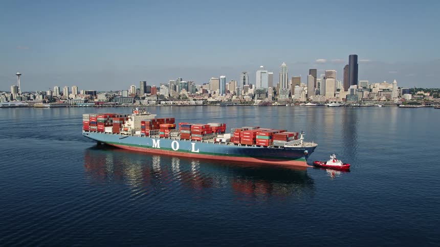 A cargo ship and tugboat sail towards the Downtown Seattle skyline on a sunny day in Washington showcasing the cityscape and transportation on Puget Sound