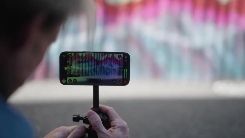 A man is holding his cell phone on a stand and he bends it down and back up as the wall in front of him is on his phone camera screen
