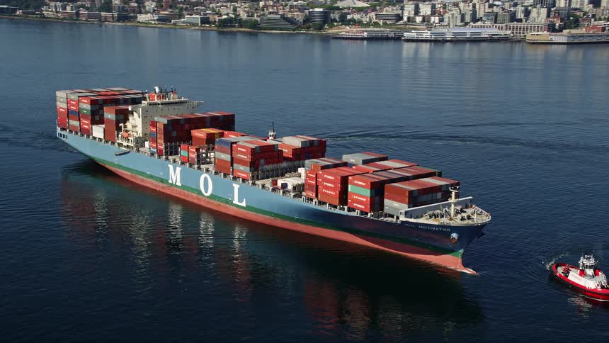 Aerial footage of cargo ships and tugboats orbiting Elliott Bay in Seattle showcasing the maritime transportation and sunny shoreline of the Pacific Northwest