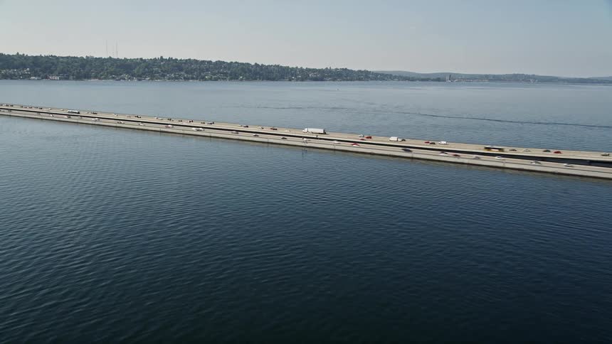  aerial footage captures traffic crossing a highway over water from a residential area towards downtown Seattle showcasing the city skyline and the Mercer Island bridge spanning Lake Washington