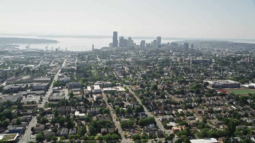 Aerial shot revealing urban homes in densely packed residential area and distant metropolitan skyline in Central Seattle Washington