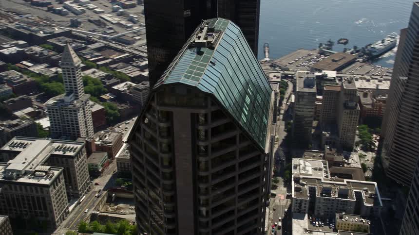 Aerial footage of Seattle Municipal Tower in downtown Seattle Washington as the camera orbits the roof showcasing the city's high-rise buildings and the vibrant metropolis below on a sunny day