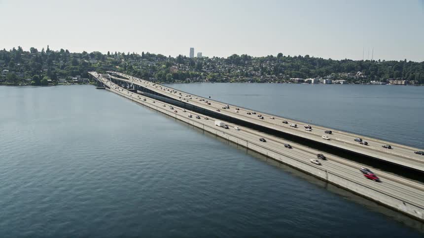 Aerial footage of traffic crossing the highway over the water revealing a residential neighborhood and the distant city skyline