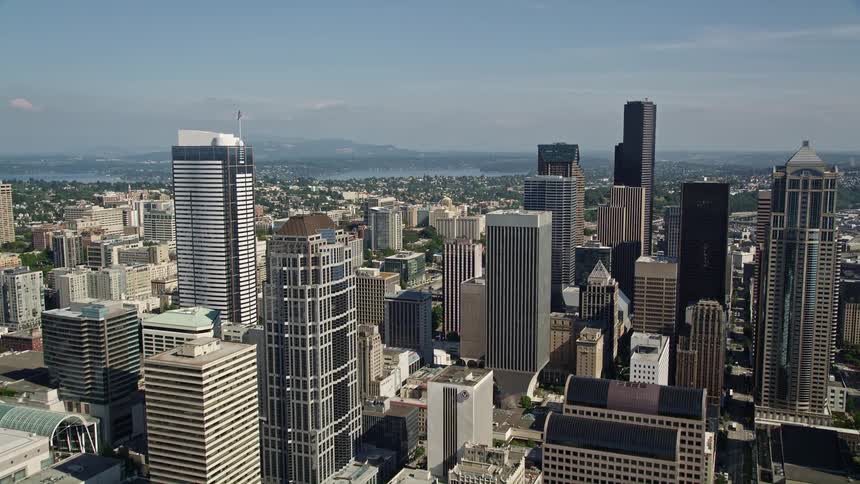 Aerial footage showcasing tall buildings filling the downtown area of Seattle focusing on the intersection beside the Seattle Public Library on a sunny day