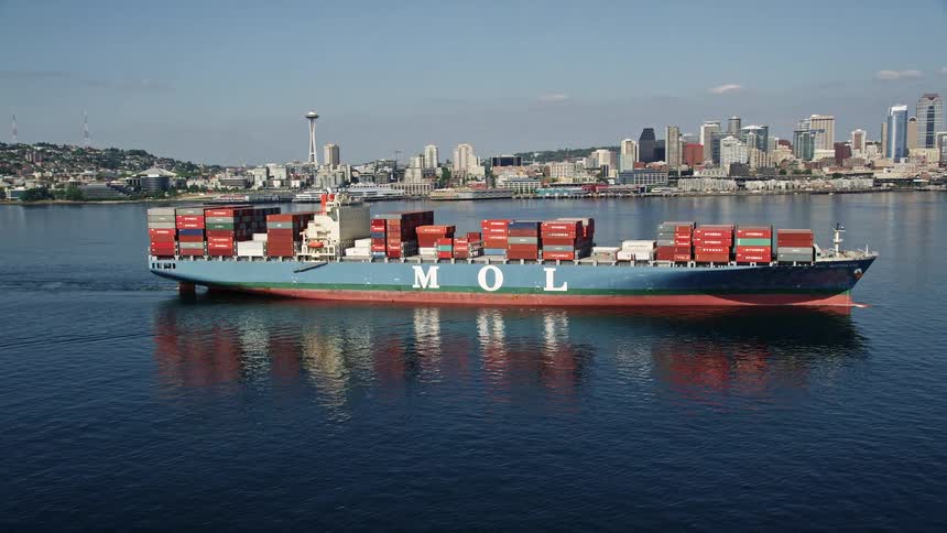 A stunning aerial view of a cargo ship sailing through Elliott Bay with the iconic downtown Seattle skyline in the background during a sunny day