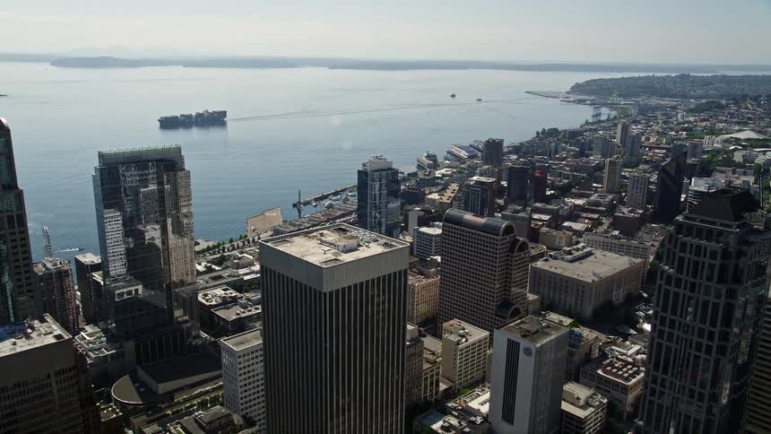 Approaching Rainier Tower and flying over skyscrapers towards the bay in downtown Seattle Washington on a sunny day with ships and high-rises in view