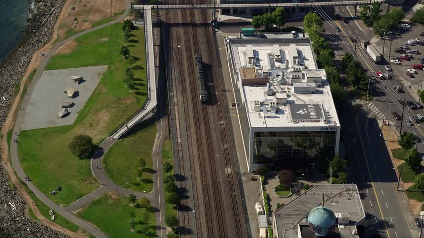 Aerial view of a commuter train passing through Myrtle Edwards Park in Downtown Seattle Washington with cars driving along the highway near the Seattle Waterfront