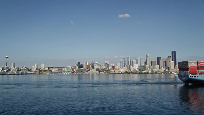 A low flying aerial shot captures a cargo ship sailing across the water revealing the stunning metropolitan city of Seattle in the distance