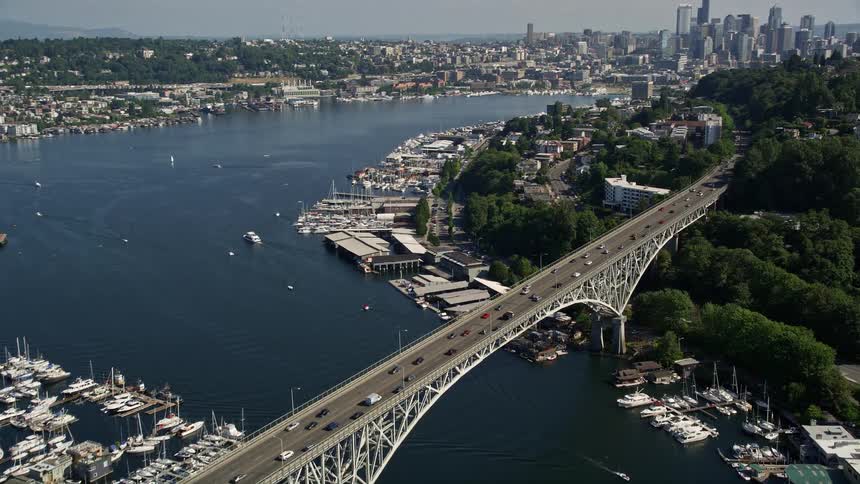 Aerial footage of a bridge spanning Lake Union approaching and flying over it to reveal the downtown Seattle skyline Washington on a sunny day