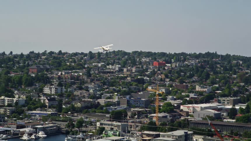 Tracking a seaplane across Fremont Cut revealing Queen Anne neighborhood in sunny Washington as boats sail and traffic moves across the bridge