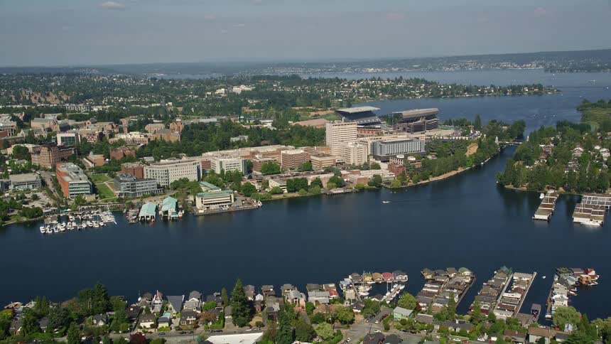 Aerial footage capturing the University of Washington and Portage Bay in Seattle Washington as boats sail in the river and traffic moves across a bridge towards suburban neighborhoods