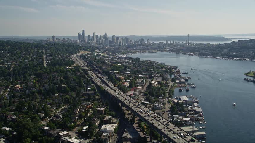 Fly over the Ship Canal Bridge and approach the Downtown Seattle skyline and Lake Union Washington capturing the high rise buildings heavy traffic and sunny cityscape