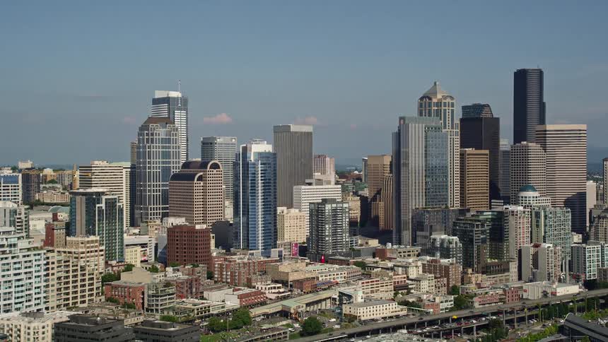 Low altitude aerial approach to Seattle Waterfront piers and skyline showcasing the metropolitan cityscape and busy harbor during the day