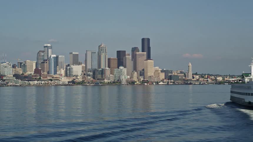 A ferry sails toward the Downtown Seattle skyline with a side view perspective and low altitude flight descending over Elliott Bay in Washington State