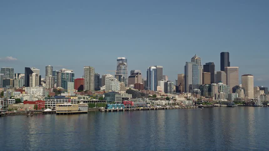Aerial footage of a low altitude approach to the Seattle Waterfront piers and skyline showcasing the high rises and bustling harbor of Downtown Seattle Washington