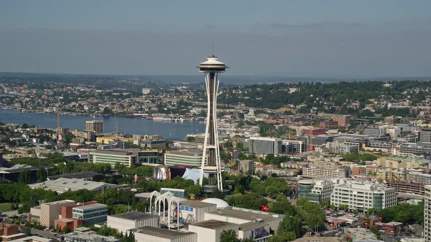 Fly high above the downtown buildings and Seattle Waterfront piers revealing the iconic Space Needle in Downtown Seattle Washington on a sunny day