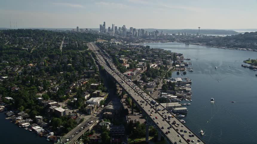 Aerial footage of cars traveling over a bridge in the city revealing the picturesque Lake Union Downtown Seattle skyline and the bustling metropolis of Washington