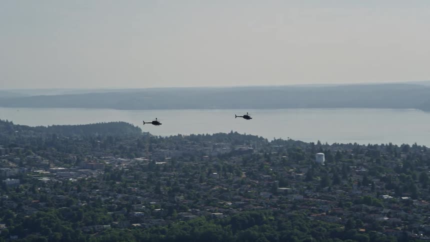 Two Kiowa Warrior helicopters fly in formation over the sunny city of Seattle Washington showcasing the power and grace of military aircraft