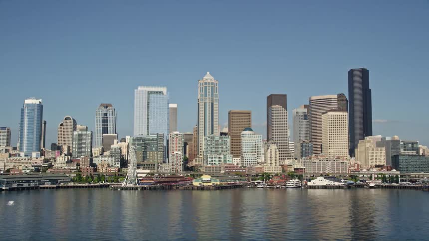 A stunning aerial view of downtown Seattle Washington showcasing tall towers and skyscrapers along the central waterfront with the Seattle Aquarium and the Seattle Great Wheel visible as boats sail in the water and traffic moves on the highway