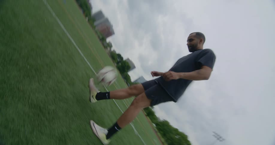 A man juggles a soccer ball with his feet on a soccer field on a cloudy day