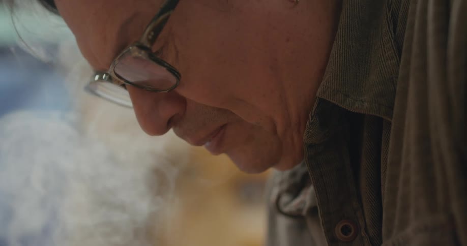 Older man focused downward as smoke rises past his face