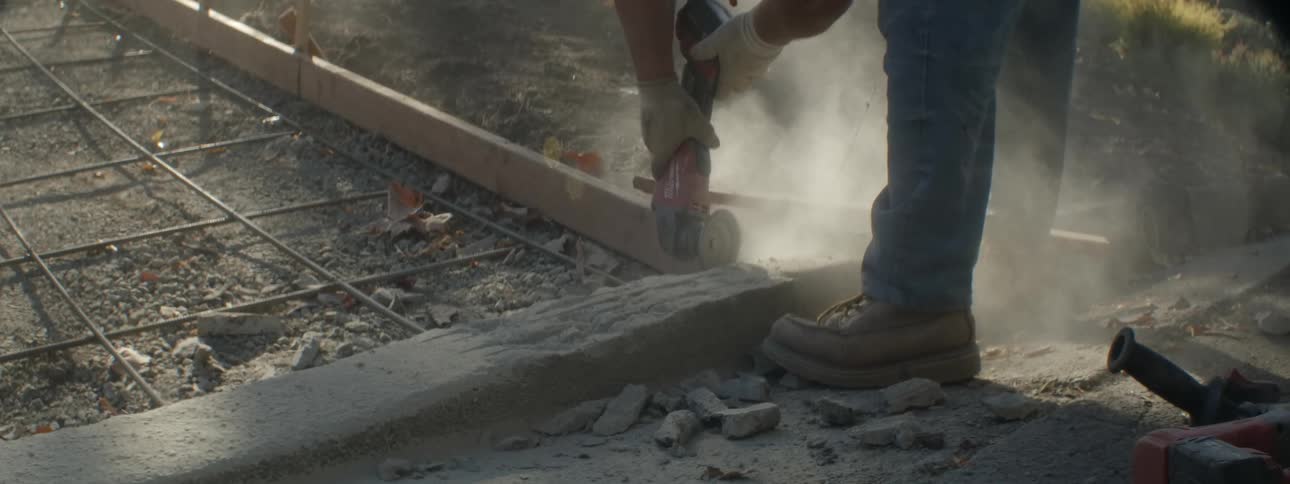 Man uses power tool to smooth curb at base of frame prepared for driveway pouring