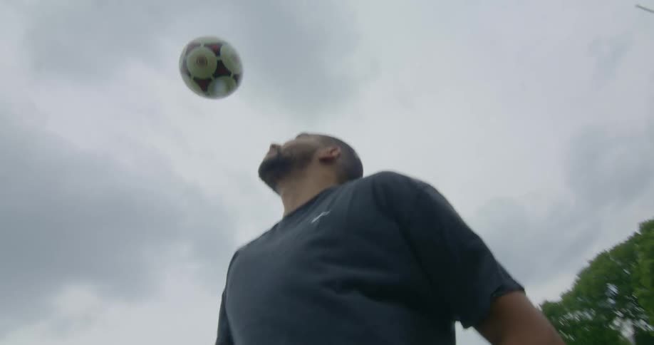 A man is bouncing a soccer ball on his head