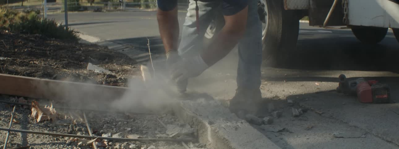 A man uses a sander to sand down wood at the end of a driveway
