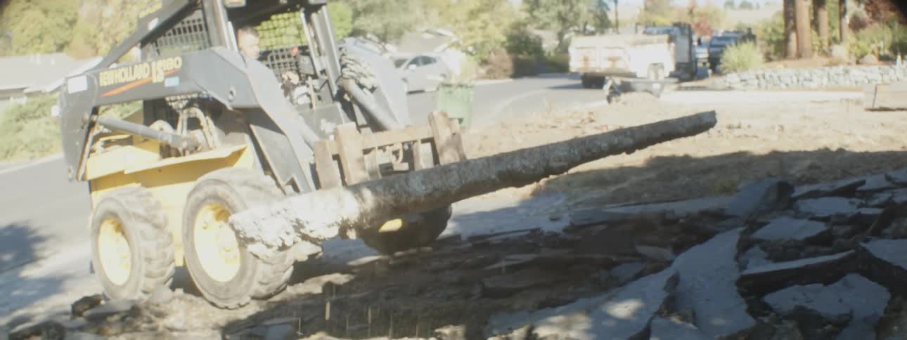 A man uses a bulldozer to remove parts of a driveway from a home
