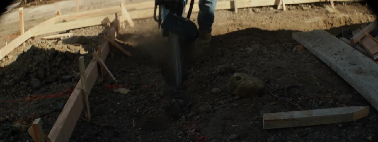 A large drill held by a man making a hole in a dirt floor