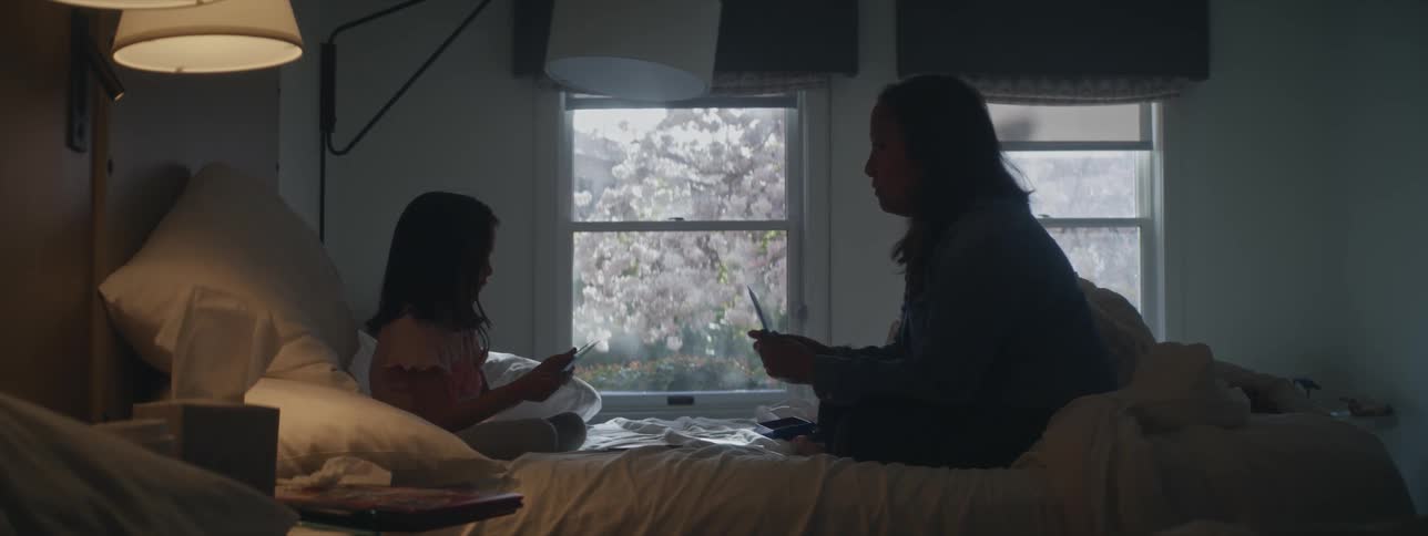 Mother and daughter sit on bed and play together in dimly lit bedroom