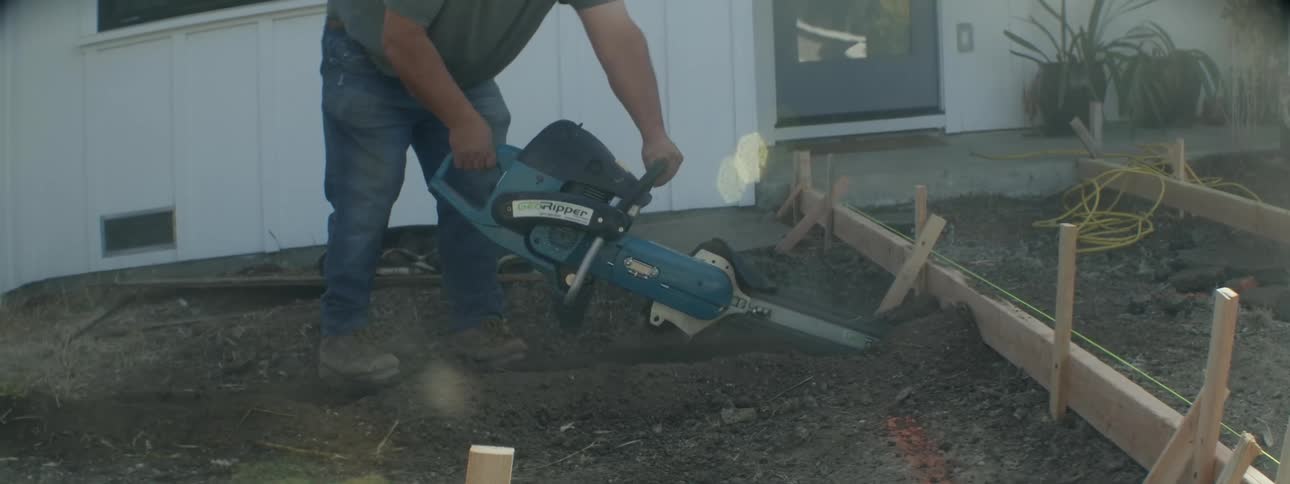 A man uses a saw to irrigate dirt in front of a house