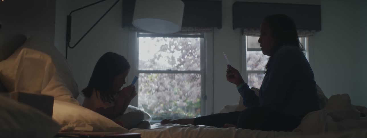 A girl and her mother play cards while sitting in bed